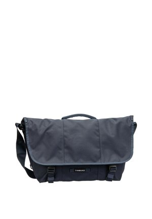 Bolsa tipo mensajero azul oscuro con correa de hombro ajustable, asa superior y dos cierres de hebilla, etiquetada con "TIMBUK2" en la parte frontal.