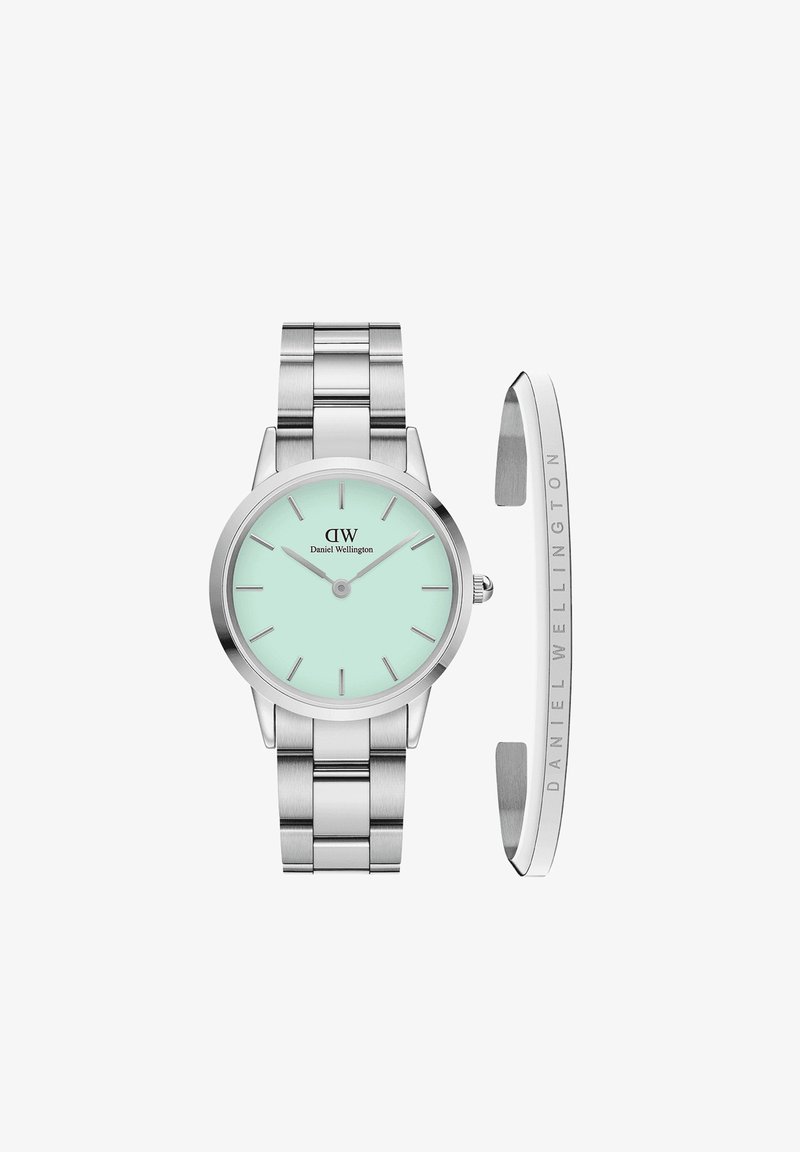 Hõbedane roostevabast terasest kell, millel on ümmargune piparmündiroheline sagedus, peened numbrid ja harjatud metallist käevõru. Kaasas on poleeritud hõbedane mansett.