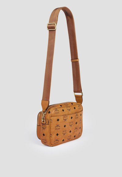 Sac bandoulière en cuir beige avec une sangle en tissu marron réglable, des accessoires en métal doré et un motif répétitif de logo MCM noire.