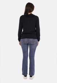 Maglione nero con collo a lupetto e maniche lunghe, abbinato a jeans svasati blu scuro. Le scarpe sono bianche con accenti neri, con una texture minima visibile.