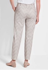 Helle beigemfarbene Hose mit einem strukturierten, abstrakten Muster, im schmalen Schnitt und mit elastischem Bund, kombiniert mit weichen beigen Schuhen.