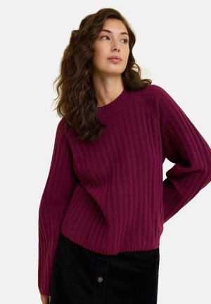 Maglione aderente a coste in un profondo bordeaux, con scollatura a girocollo e maniche lunghe, abbinato a pantaloni in velluto corduroy neri.