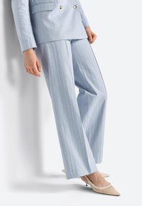 Hellblau gestreifter Anzug mit doppelreihigem Sakko und weit geschnittenen Hosen, kombiniert mit beigen Slingback-Absätzen. Glatte Stoffstruktur.