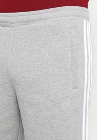 Close-up of light grey sweatpants with white side stripes and pocket, worn with a red top.