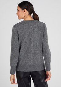 Pull en tricot gris à manches longues, avec des poignets et un ourlet côtelés. Texture douce, col rond, design minimaliste, présenté de dos.