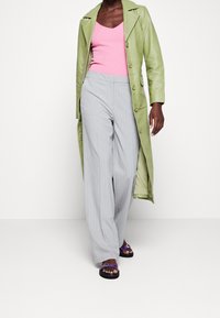 Długi zielony skórzany płaszcz, różowy prążkowany top na ramiączkach, szare szerokie spodnie w prążki i fioletowe sandały z czarnymi podeszwami.