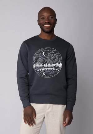 Dunkelblaues Sweatshirt mit einem runden weißen Grafikdesign, das Berge, Bäume und einen Mond auf der Vorderseite darstellt. Aus Baumwollmaterial mit einem gerippten Rundhalsausschnitt.