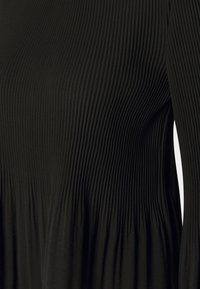 Abito nero a coste con maniche lunghe, caratterizzato da una trama verticale e un corpo aderente che si allarga sui fianchi. Tessuto liscio con una finitura morbida.