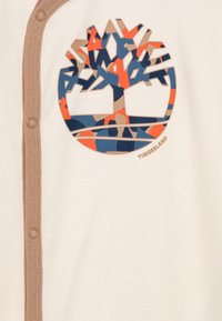 T-shirt in tessuto bianco con logo ad albero Timberland multicolore in tonalità di arancione, blu e beige, completo di chiusura con bottoni a pressione marroni.