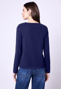 Dunkelblauer Strickpullover mit langen Ärmeln, runder Halslinie und geradem Schnitt, kombiniert mit jeansblauen Hosen. Glatte Textur.