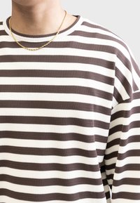 Bruin en witte gestreepte trui van een gestructureerde stof, met een geribbeld decolleté en een comfortabele pasvorm. Een gouden ketting zichtbaar.