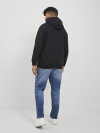 Black hoodie with a drawstring hood, paired with light blue denim jeans and white sneakers; displayed from the back against a white background.
