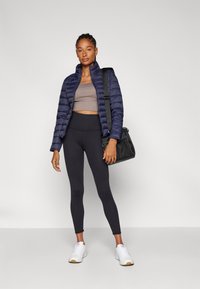 Doudoune navy, crop top beige, leggings noirs, baskets blanches et sac noir. Design élégant avec une texture lisse et une coupe ajustée.