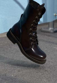 Stivaletto in pelle marrone con lacci, finitura lucida, punta tonda, cuciture rinforzate e suola testurizzata. Design elegante, occhielli stilosi.