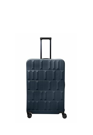 Grande valise rigide bleu foncé avec motif géométrique, poignée rétractable et quatre roues pivotantes sur fond blanc.
