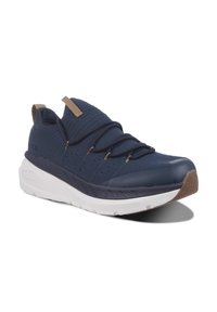 Marineblå strikkede sneakers med elastiske snørebånd og en tan-farvet accent. Har en tyk hvid sål med en tekstureret brun gummi tåkap og detaljer på siden.