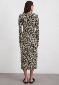 Mustapituinen pitkähiha dressi, jossa on kerma-värinen kukkakuosi, polvipituinen, vartalonmyötäinen siluetti, pyöreä kaula-aukko ja pehmeä kankaan rakenne.