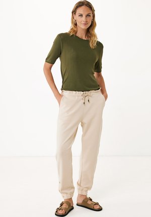 Olivgrüner Strickpullover, hellbeige Jogginghose mit elastischen Bündchen und braunen Sandalen. Verfügt über einen Kordelzug an der Taille und Knopfdetails an der Hose.