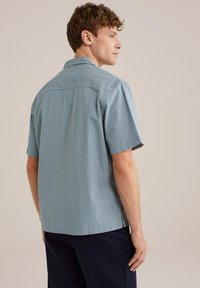 Camicia a maniche corte in blu chiaro e bianco a righe verticali. Presenta un colletto classico e una trama sottile, con un orlo dritto in vita.