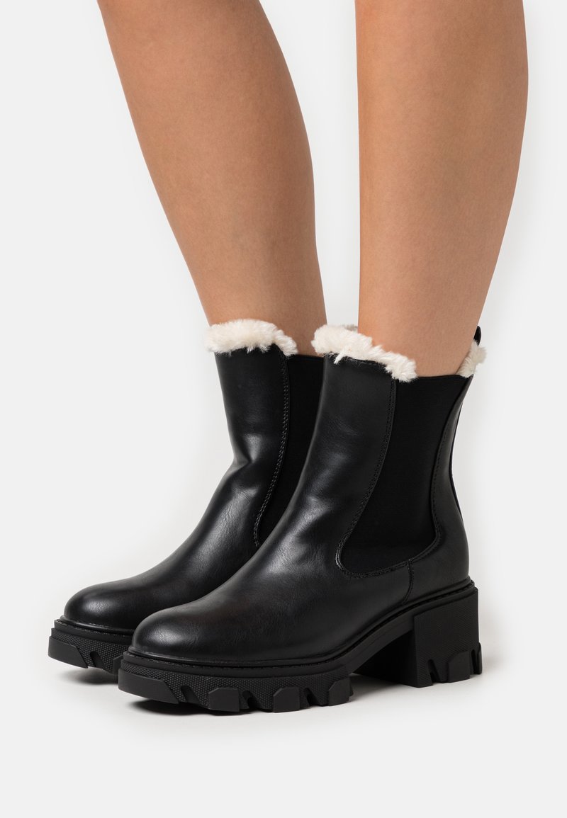 Bottines en cuir noir avec une bordure en fausse fourrure au col, des panneaux latéraux élastiques et des semelles en caoutchouc noir texturé et épais.