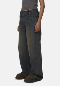 Jeans en denim à jambes larges de couleur bleu foncé avec une finition délavée, dotés de cinq poches, de coutures visibles et d'une fermeture à bouton classique.