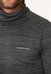 Grå langærmet skjorte med høj krave, lavet af struktureret stof, med et diskret vandret stribemønster og et hvidt "ENDURANCE" logo på brystet.