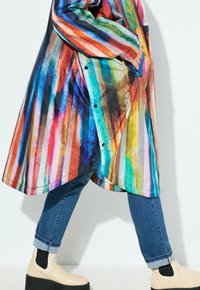 Veste colorée et surdimensionnée avec des motifs rayés rouges, bleus, verts, oranges et jaunes. Tissu lisse avec un ourlet arrondi et des boutons décoratifs.