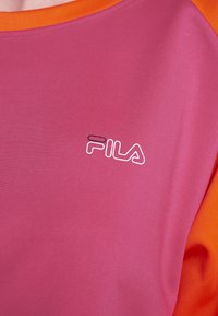 Rosa Kurzarmhemd mit orangefarbenem Kragen, aus glattem Stoff. Mit einem weißen FILA-Logo auf der Brust.