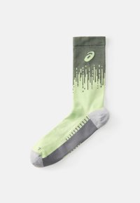 Calcetín verde y verde claro con un diseño degradado, que presenta patrones de puntos, secciones de talón y punta en gris, y un logo cerca de la parte superior.
