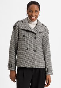 Houndstooth-patterned double-breasted jacket in black and white, featuring large buttons, epaulets, and cropped sleeves with buckle accents.