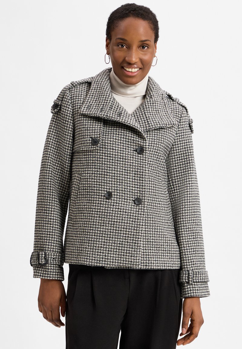 Houndstooth-patterned double-breasted jacket in black and white, featuring large buttons, epaulets, and cropped sleeves with buckle accents.
