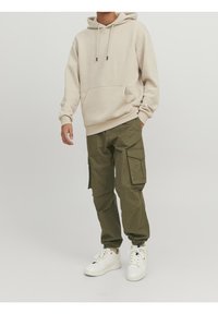 Beige katoenen hoodie met een voorzak en een trekkoord, gecombineerd met olijfgroene cargobroeken met zijzakken. Draag met witte sneakers.