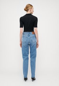 Μαύρο κοντομάνικο εφαρμοστό τοπ συνδυασμένο με ψηλόμεσα ανοιχτό μπλε τζιν. Τα τζιν διαθέτουν καφέ δερμάτινη ραφή, ελαφριά φθορά και ίσια γραμμή.