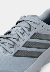 Αθλητικό παπούτσι ανοιχτού γαλάζιου χρώματος με επάνω μέρος από υφασμένο πλέγμα με υφή, τρεις γκρι ρίγες και αντίθετα λευκά κορδόνια, με μαξιλαρωμένη σόλα.