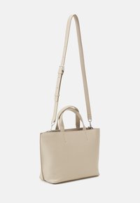 Sac cabas en cuir beige à la forme structurée. Il possède des poignées courtes et une bandoulière amovible et réglable. Fermeture supérieure zippée.
