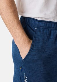 Marina blå sportshorts i texturerat tyg, med elastisk midja, sidoficka och en liten svensk flagga som accent.