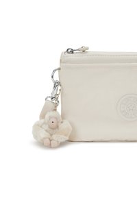 Borsa in nylon beige con chiusura a zip, caratterizzata da un logo rotondo. È attaccato un morbido charm a forma di scimmia con base beige e dettagli bianchi.