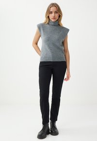Grauer ärmelloser Rollkragenpullover aus weichem Strickmaterial, kombiniert mit schwarzen Slim-Fit-Hosen und schwarzen Schnürstiefeln. Einfaches und minimalistisches Design.