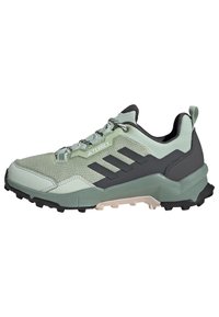 Zapatillas deportivas verde claro con una parte superior de malla texturizada, acentos negros, tres rayas paralelas y una suela robusta diseñada para tracción al aire libre.