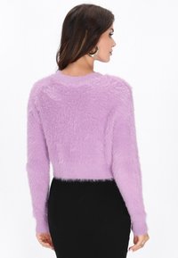 Maglione di un leggero viola, peloso, con maniche lunghe, scollo rotondo e design cropped, abbinato a una gonna nera aderente.
