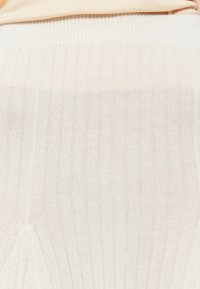 Light cream ribbed knit fabric featuring vertical stripes and a subtle texture, with a smooth finish along the hemline.