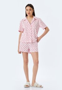 Vaateyhdistelmä, jossa on vaaleanpunainen lyhythihainen pyjama, jossa on punaisia sydänkuvioita. Mukana on napillinen paita ja yhteensopivat shortsit. Pehmeä kangas ja rento istuvuus.