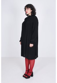 Zwarte jurk met lange mouwen, een gerimpelde buste en een losse pasvorm. Draagt met rode maillots en zwarte platform schoenen. Eenvoudig ontwerp, geen patronen.