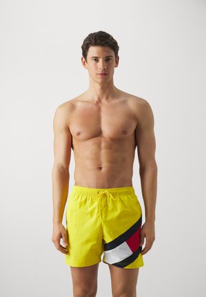 Pantaloni da nuoto gialli con vita elastica, caratterizzati da un motivo diagonale in nero, rosso e bianco. Tessuto liscio, design fino al ginocchio.
