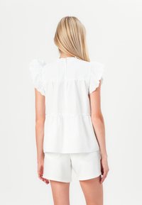 Balta peplum blūze, izgatavota no viegla auduma, ar volānu piedurknēm, saburzītu jostu un apaļu dekoltē. Apvienota ar baltām šortiem.