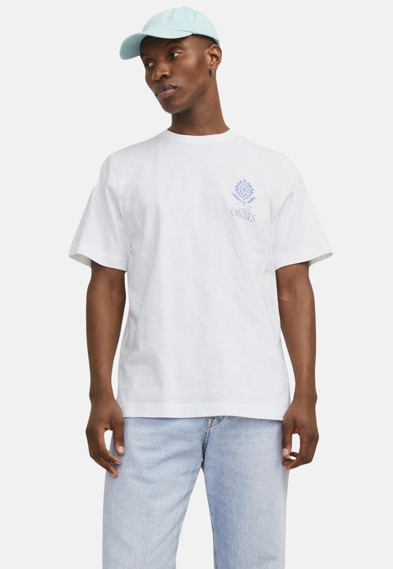 Weißes Baumwoll-T-Shirt mit kurzen Ärmeln, mit einem hellblauen Logo und Design auf der linken Brust. Das Modell trägt eine hellblaue Cap und Jeans.