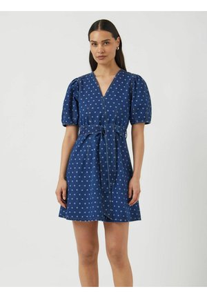 Robe en denim bleu foncé avec des pois bleu clair, manches courtes avec volants, décolleté en V et ceinture à nouer à la taille. Coupe droite, au-dessus du genou.