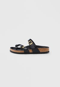 Μαύρο πέδιλο ανοιχτού δαχτύλου με σόλα από φελλό και δύο ρυθμιζόμενους μαύρους ιμάντες με χρυσές αγκράφες, εμφανιζόμενο σε πλάγια όψη σε λευκό φόντο.