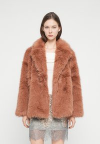 Καφέ μπουφάν από ψεύτικη γούνα με φαρδύ γιακά, διπλή σειρά κουμπιών και άνετη σιλουέτα, συνδυασμένο με φούστα από δαντέλα με παγιέτες.