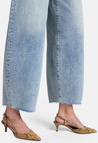 Slingbackklackar med spetsig tå i gult ormskinnstrykt material, parat med ljusblå vida jeans i denim med fransade detaljer.